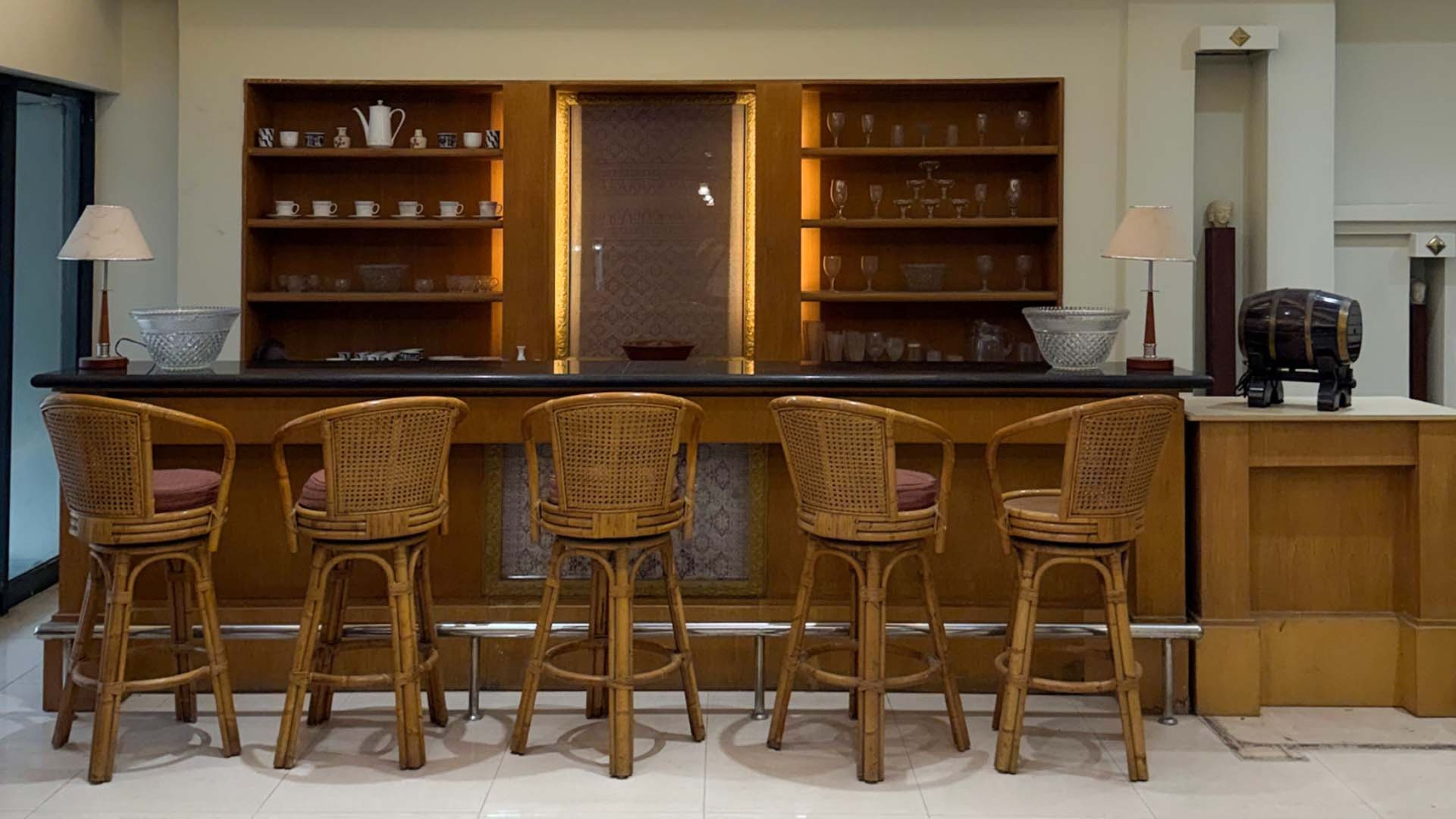 A bar area with four wicker chairs, a counter with a glass bowl, and shelves with various glassware.
