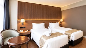 Een hotelkamer met twee bedden, een houten hoofdeinde, nachtlampjes, een klein rond tafeltje en een stoel.