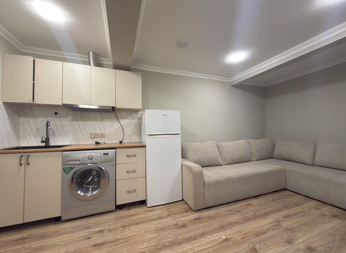A compact kitchen with a washing machine, a refrigerator, and a beige sofa.