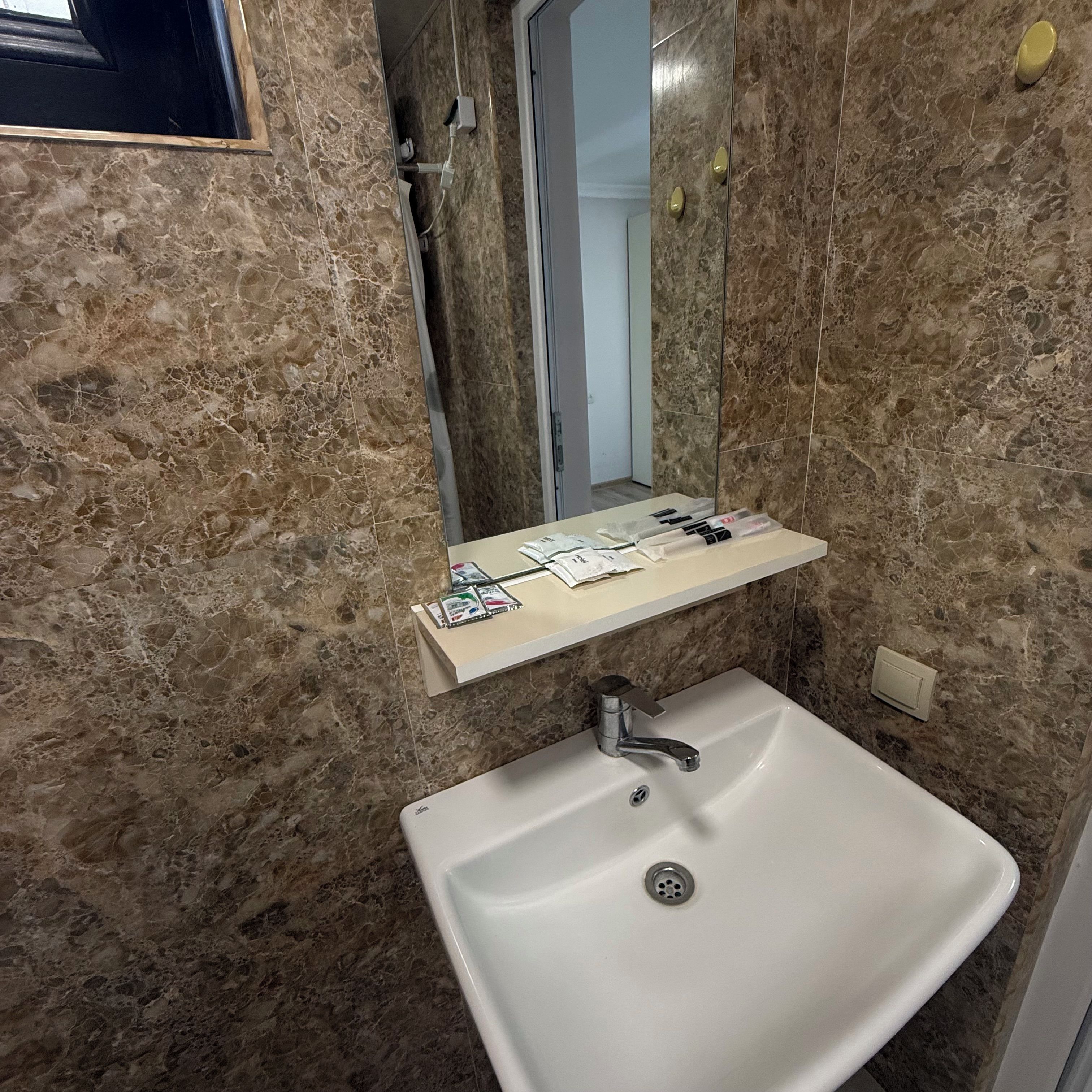 Un bagno con una parete in marmo, un lavandino e uno specchio.