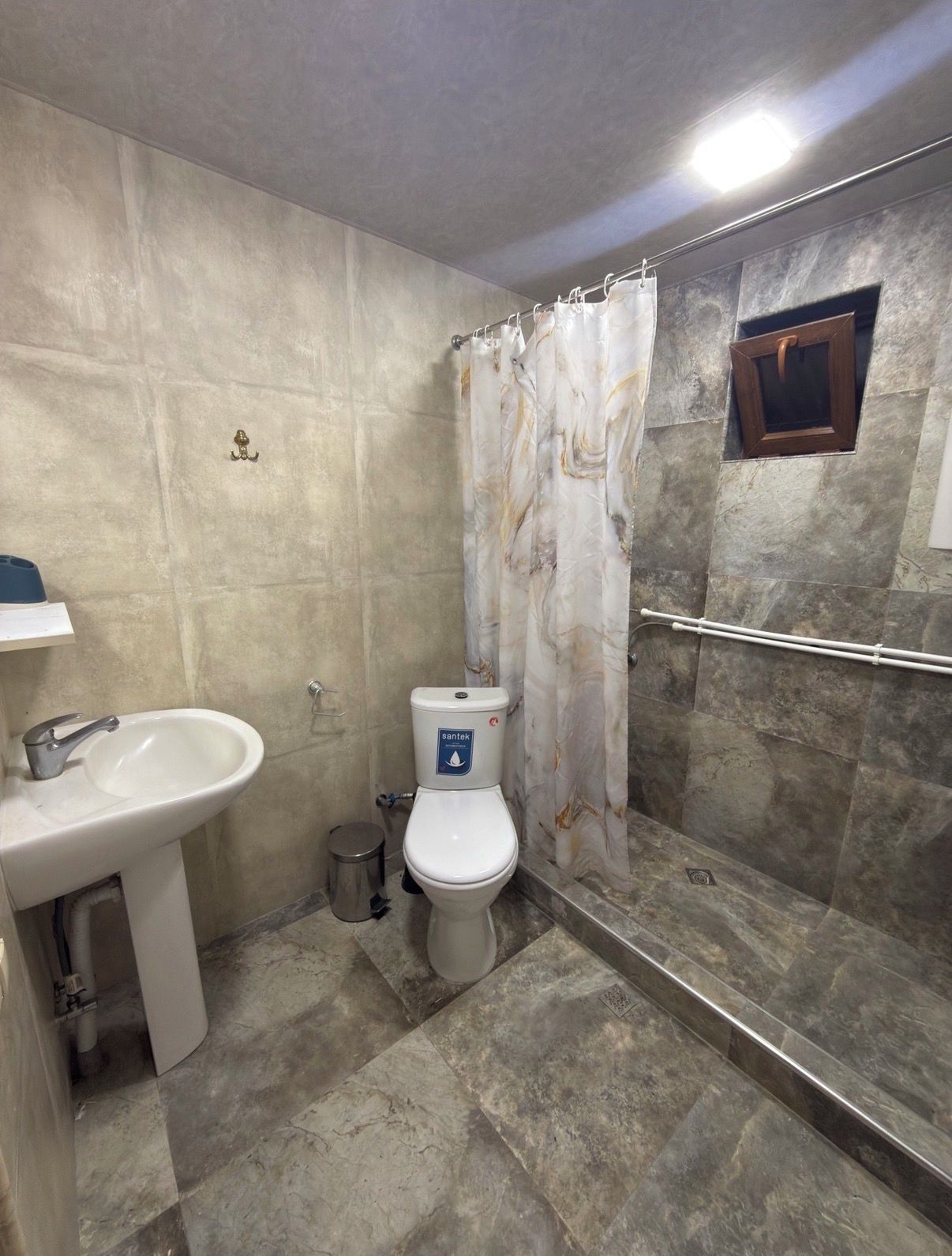 A bathroom with a toilet, sink, shower, and a small window.