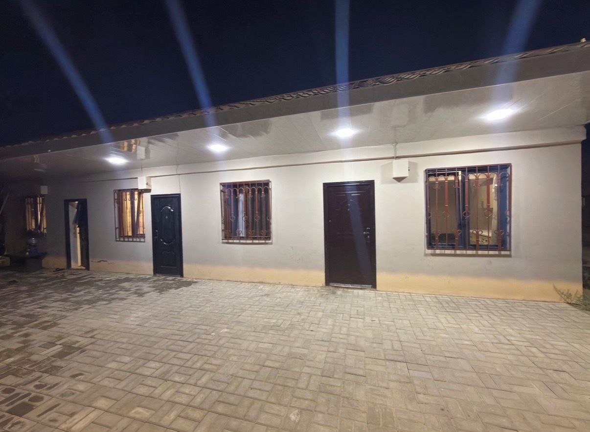 A building with multiple doors and windows, a paved ground, and a flat roof.