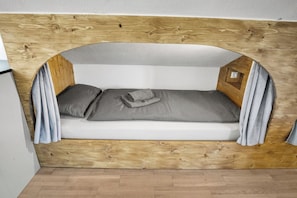 A small, cozy room with a wooden headboard, a single bed with grey bedding, and a small window with curtains. - Cozy living room with a fireplace and a tiled stove, featuring two balconies in Oberstaufen (Oberstaufen)