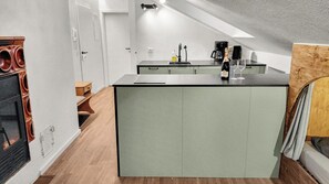 A compact kitchen with a central island, a built-in stove, and a dining area with a bench. - Cozy living room with a fireplace and a tiled stove, featuring two balconies in Oberstaufen (Oberstaufen)