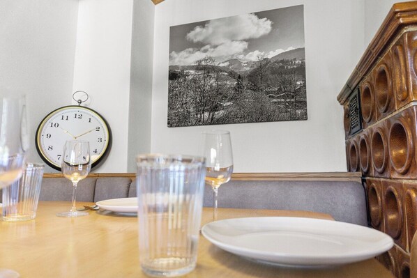 A dining table with plates and glasses, a wall clock, and a black and white photograph. - Cozy living room with a fireplace and a tiled stove, featuring two balconies in Oberstaufen (Oberstaufen)