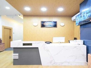 Una zona de recepción con mostrador de mármol, paneles de madera y un televisor montado.