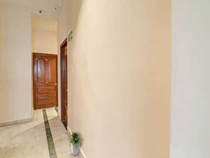 Un pasillo con una puerta de madera, una planta en maceta y piso de baldosas.