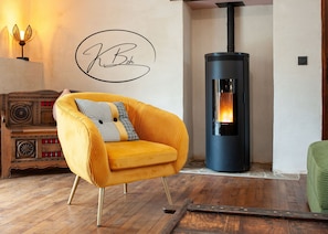 A room with a yellow armchair, a black wood-burning stove, and a decorative wall sign. - Hélène's house for 2 to 4 people with a garden, 15 minutes from the ocean (Gommenec'h)