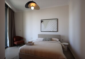A modern bedroom with a bed, a chair, a bedside table, a toilet, and a wall-mounted artwork. - Elegant 1BR apartment in Burj Vista, steps to Iconic Burj Khalifa and Dubai Mall (Dubai)