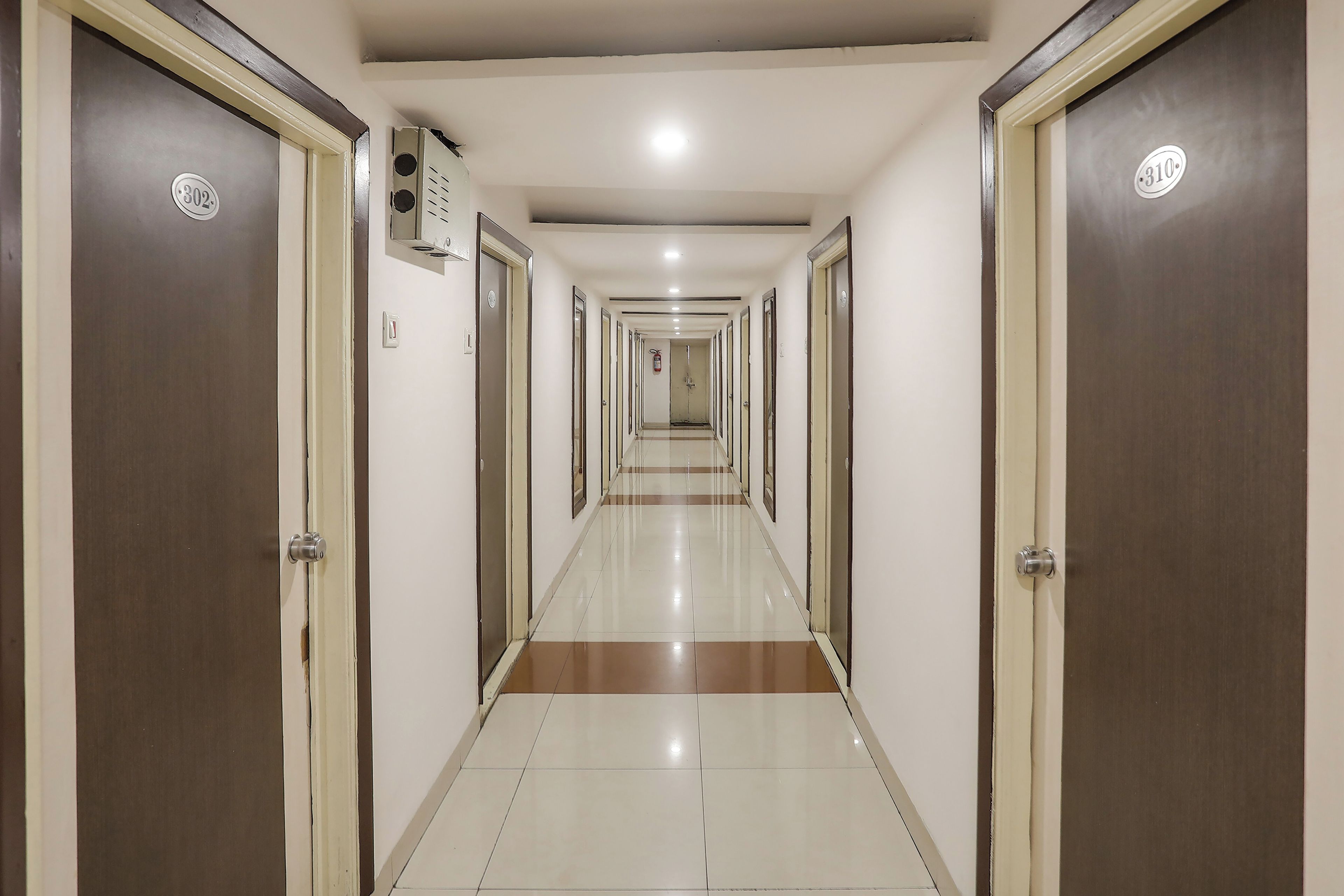 A hotel corridor with doors numbered 302 and 310, a fire alarm, and a tiled floor.