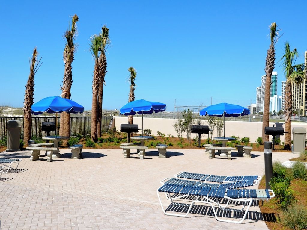 An outdoor seating area with blue umbrellas, palm trees, and a view of the city skyline.