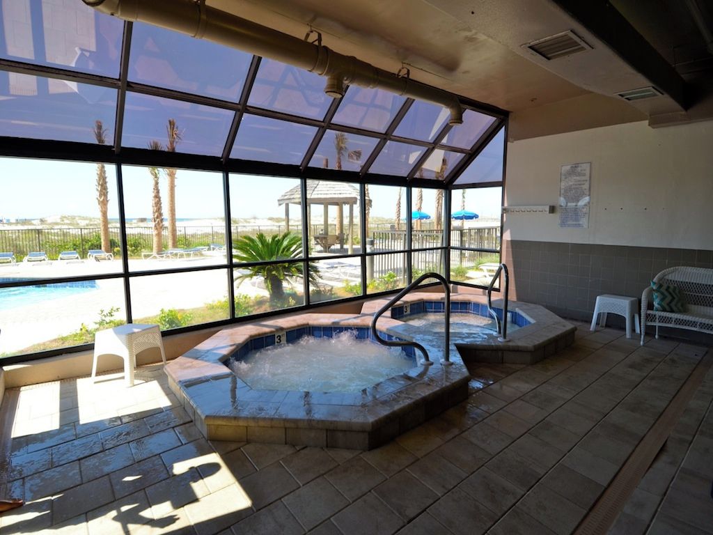 A spa area with two hot tubs, a seating area, and a view of a pool and beach.