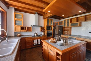 A modern kitchen with wooden cabinets, granite countertops, stainless steel appliances, and a large island. - Cozy house with a fireplace (Puerto Varas)