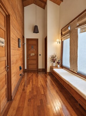 A hallway with wooden flooring, a door with a sign, a bench with a vase, and a window with blinds. - Cozy house with a fireplace (Puerto Varas)
