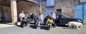 Un grup de persones al costat de motos i un cotxe davant d'un edifici de pedra amb una porta blava.