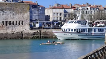 A waterfront scene with a large white boat docked at a pier, a stone wall, and buildings with red roofs in the background.
