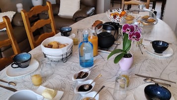 A breakfast setting with a variety of food items, a coffee maker, and a tea set on a patterned tablecloth.