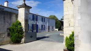 Straßenansicht eines weißen Gebäudes mit blauen Fensterläden, einem Steintor und blauem Himmel.