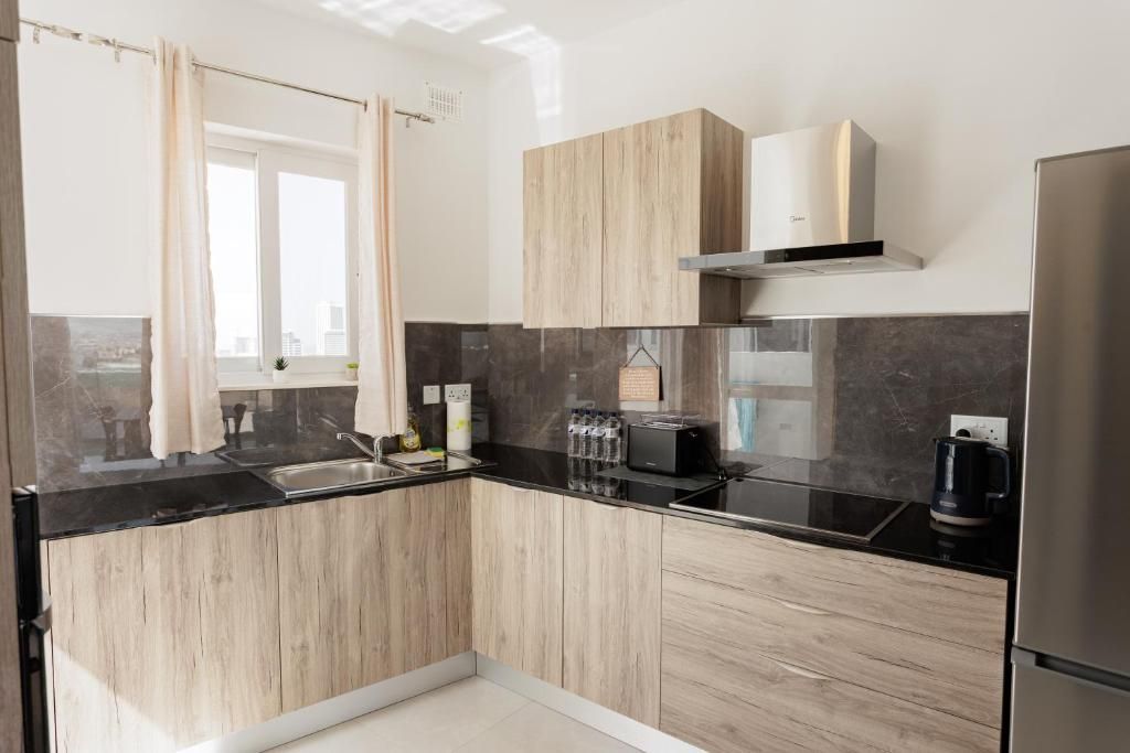 A modern kitchen with wooden cabinets, a black countertop, a built-in oven, and a stainless steel refrigerator.