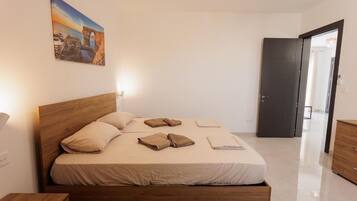 Un dormitorio con una cama de madera, una mesita de noche, un cuadro en la pared y una puerta que da a otra habitación.