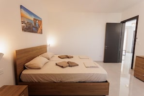 A bedroom with a wooden bed, a nightstand, a painting on the wall, and a door leading to another room.