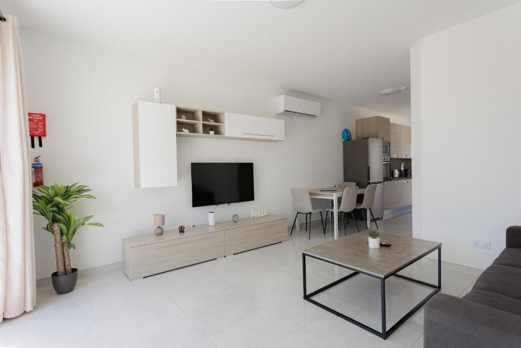 Una sala de estar moderna con una televisión de pantalla plana, un comedor y una cocina al fondo.