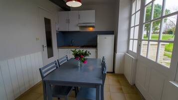 Une cuisine avec une table à manger, des chaises, un luminaire suspendu rouge et une vue sur l’extérieur grâce à de grandes fenêtres.