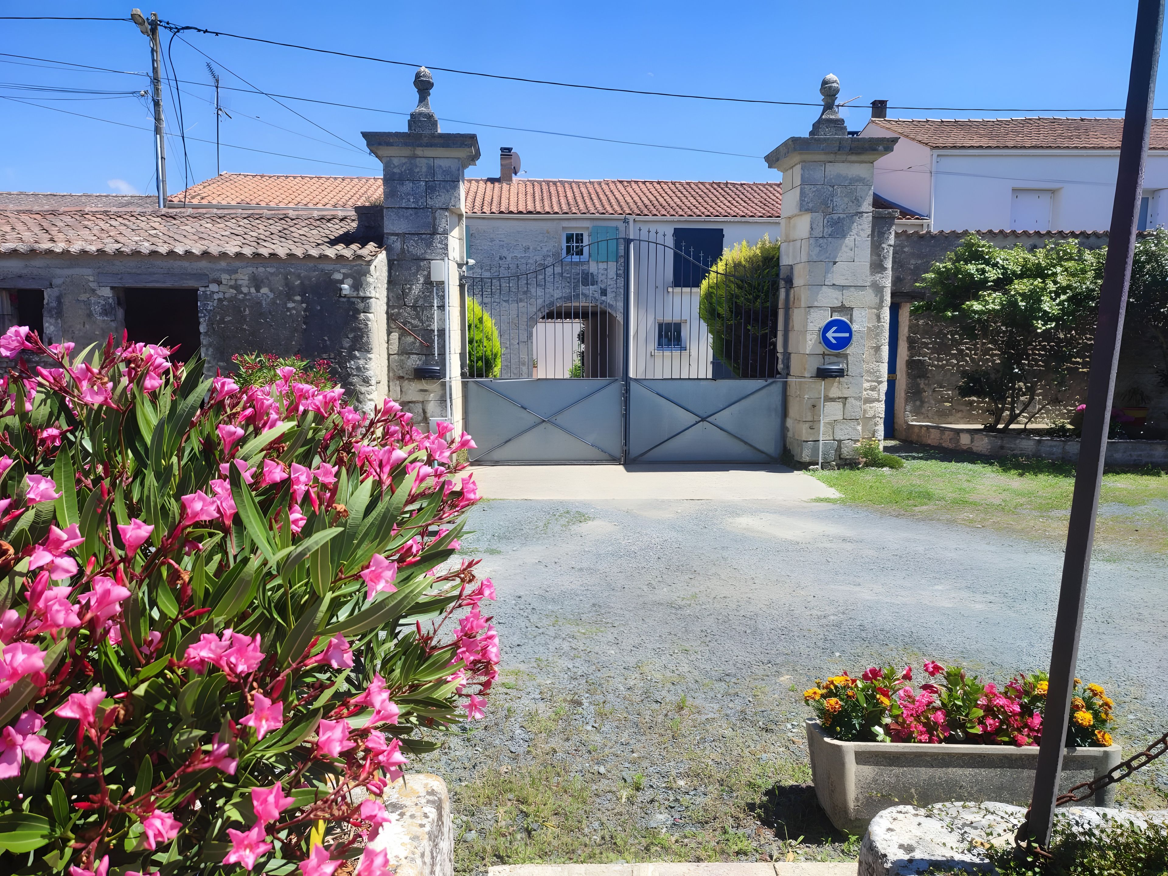 Una entrada con muro de piedra, portón metálico y señal azul indicativa.