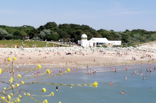 Una playa con un edificio blanco, gente tomando el sol y un cielo despejado.