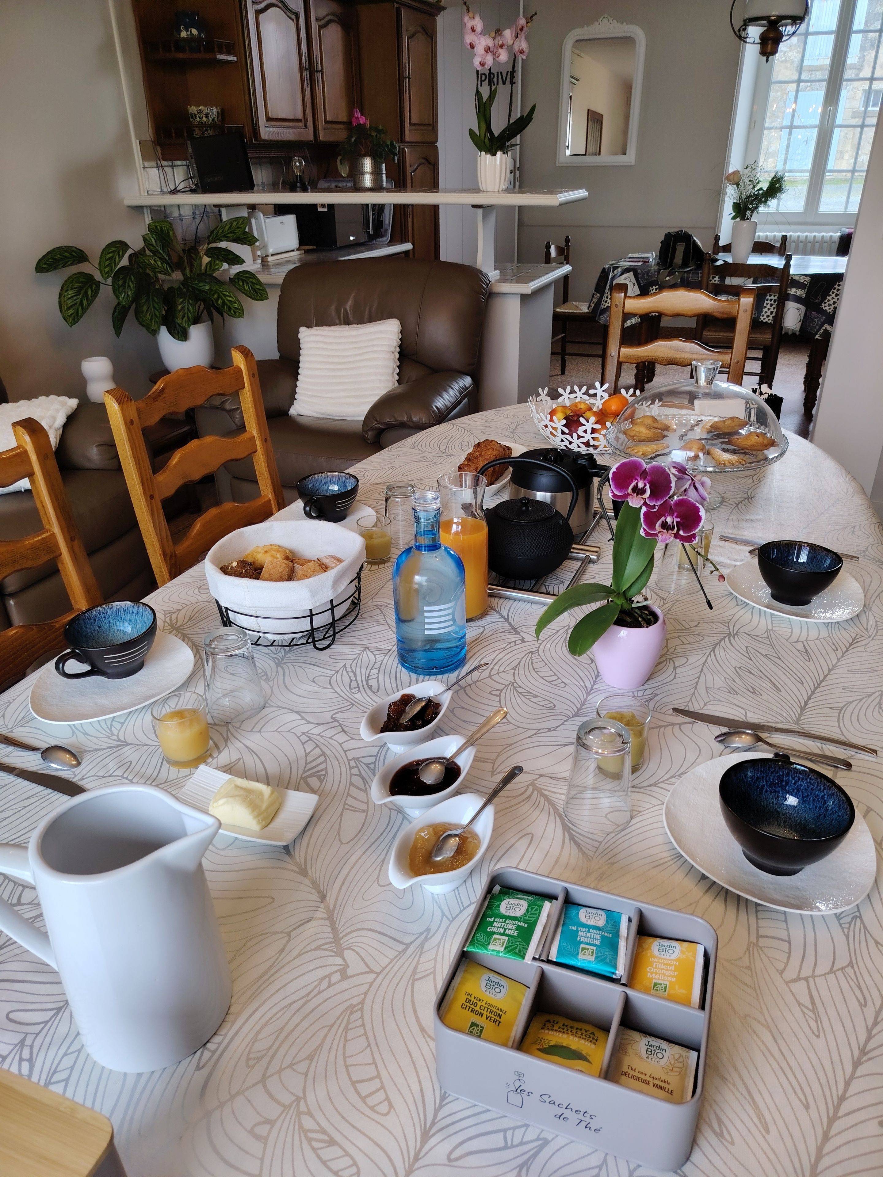 A breakfast setting with a variety of food items, a coffee maker, and a tea set on a patterned tablecloth.