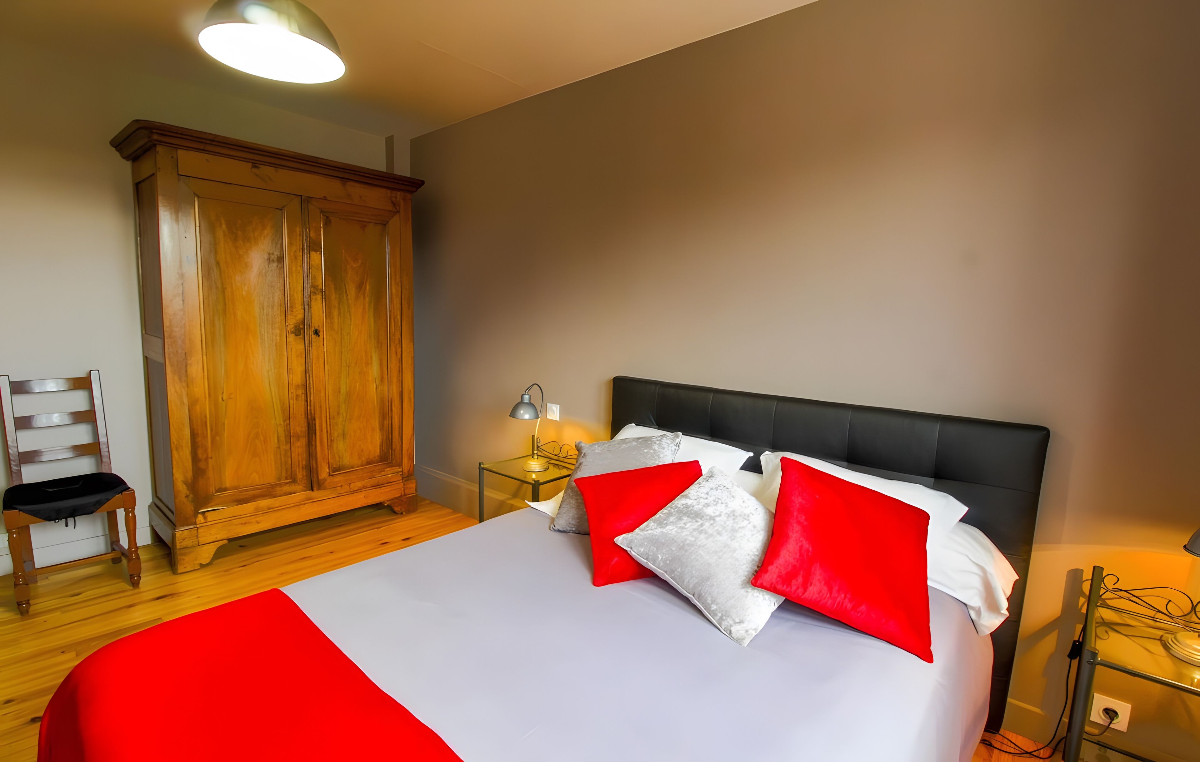 A bedroom with a bed, a wardrobe, a chair, and a bedside table with a lamp.