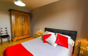 Une chambre à coucher comprenant un lit, une armoire, une chaise et une table de chevet avec une lampe.