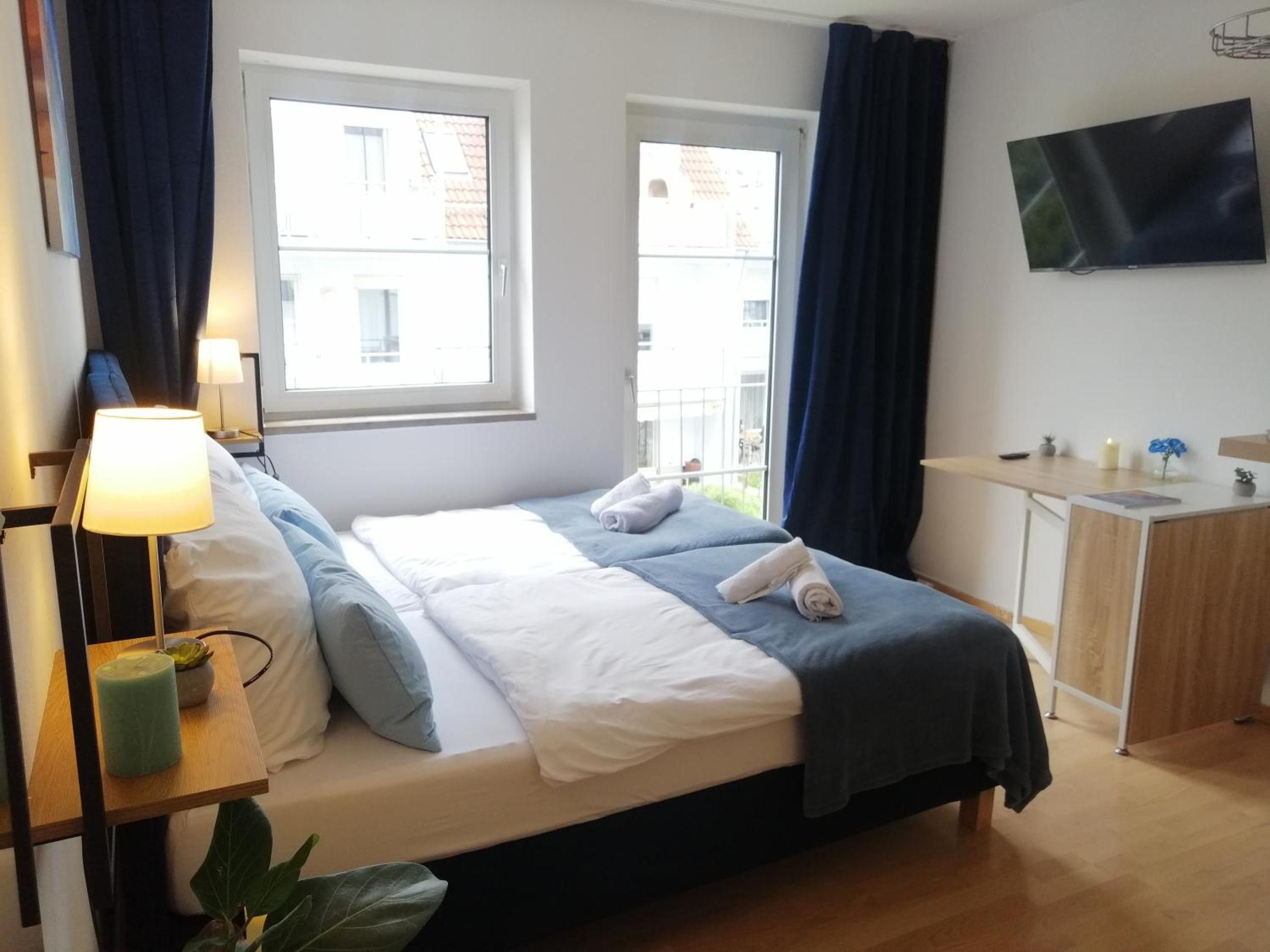A hotel room with a bed, bedside table, lamp, and a TV on the wall.