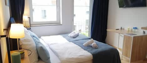 Habitación de hotel con cama, mesita de noche, lámpara y televisor en la pared.