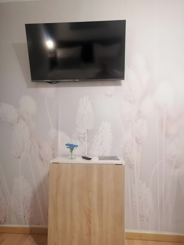 Un televisor de pantalla plana penjat a la paret, amb una taula auxiliar de fusta a la part frontal.