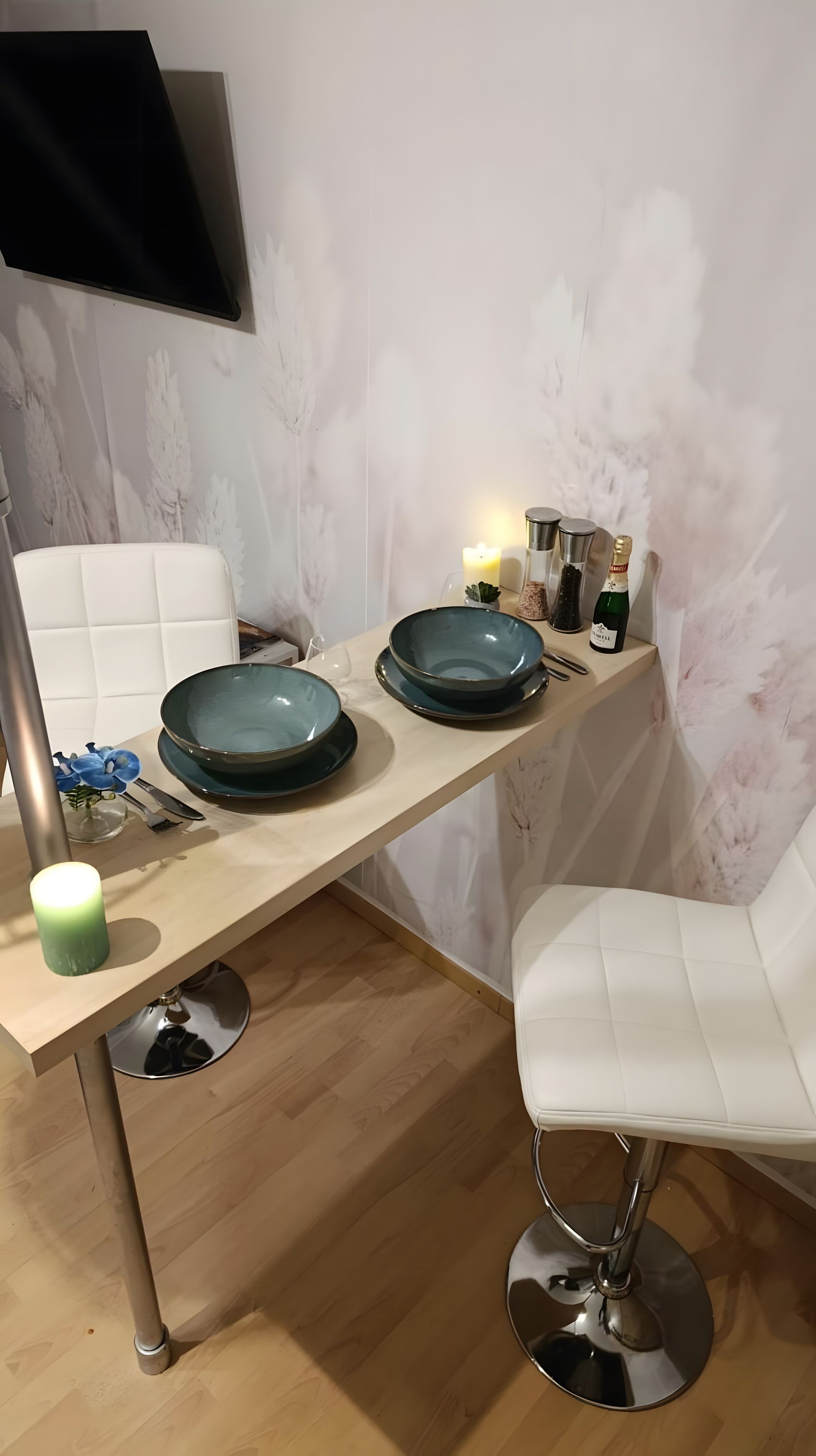 Un comedor moderno con una mesa de madera, dos platos azules, una vela verde y una silla blanca.