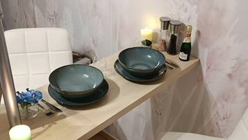 A modern dining area with a wooden table, two blue plates, a green candle, and a white chair.