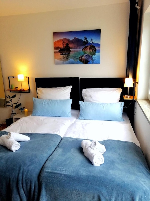 Een tweepersoonsbed met twee kussens, een nachtkastje met een lamp en een schilderij aan de muur.