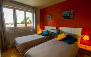 Une chambre d’hôtel avec deux lits, un mur rouge, une fenêtre et une table de chevet avec une lampe.