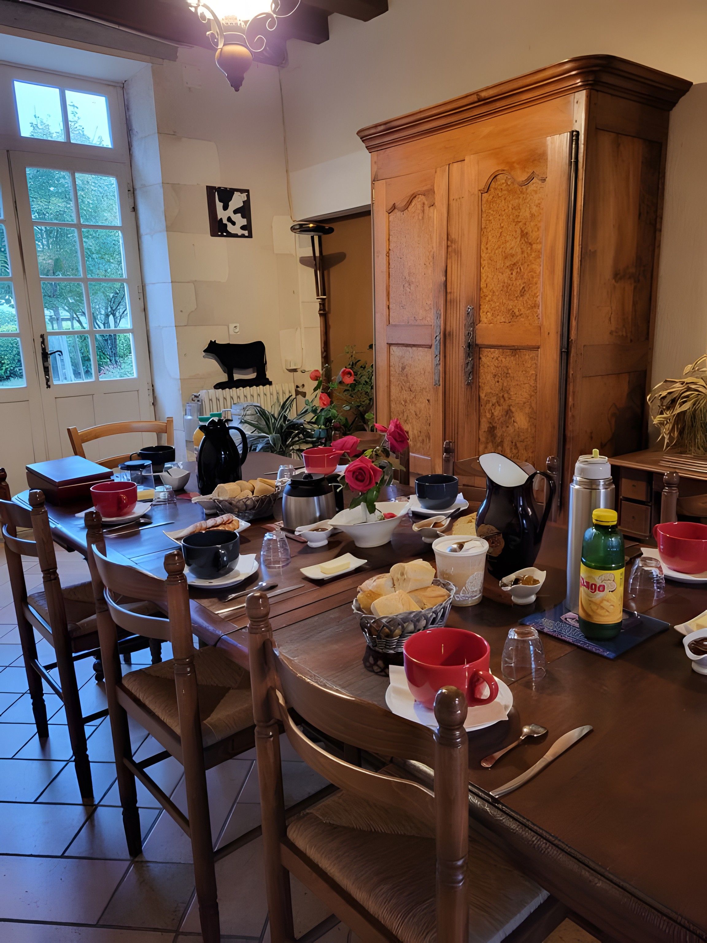 Mesa de jantar posta com diversos pratos e bebidas, cercada por cadeiras de madeira.