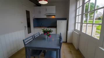 Una cocina con una mesa de comedor, sillas, una lámpara colgante roja y vistas al exterior a través de amplios ventanales.