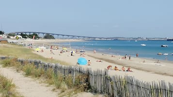 A beach with a wooden fence, people sunbathing, and a bridge in the background.