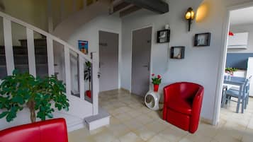 Un interior moderno con una escalera, una silla roja, una puerta blanca con la etiqueta 'WC' y un aplique de pared.