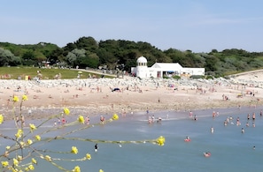 Une plage avec un bâtiment blanc, des gens qui prennent un bain de soleil et un ciel dégagé.