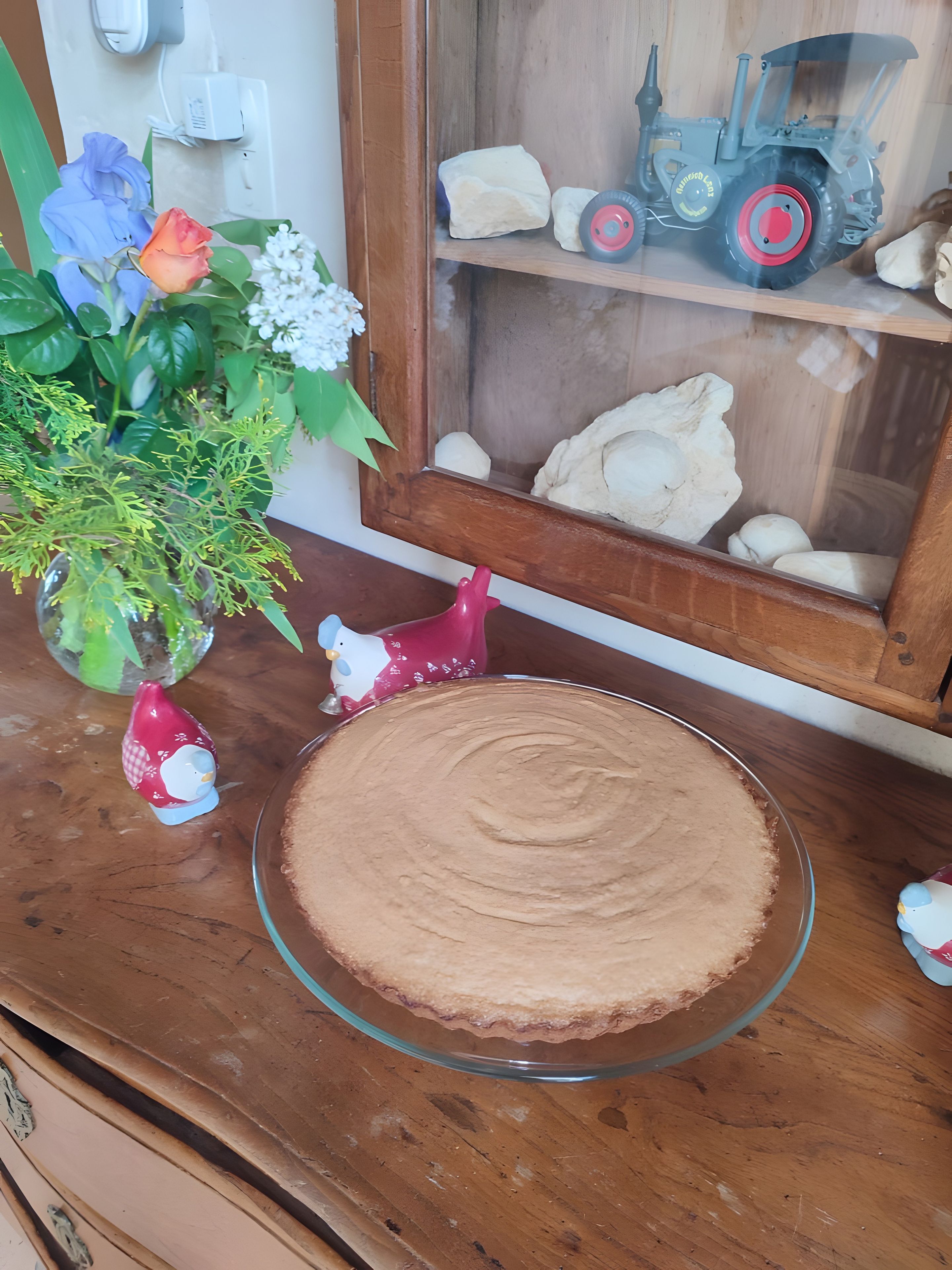 A dessert plate on a wooden table, a vase with flowers, and a toy tractor in a window.