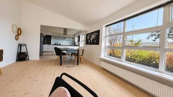 A modern interior with a dining area, kitchen, and large windows offering a view of trees.
