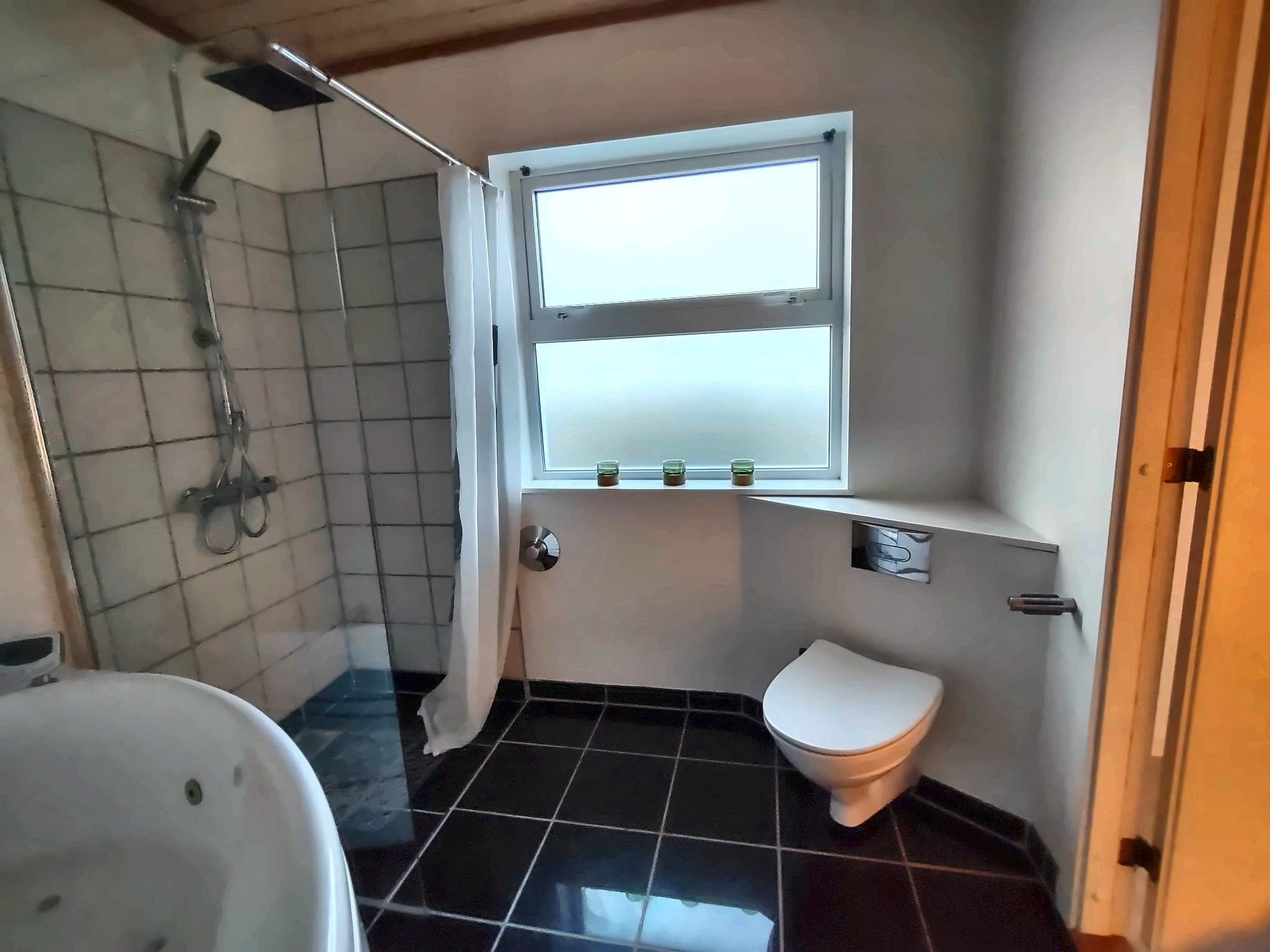 Ein kleines Badezimmer mit Dusche, Toilette und einem Fenster.