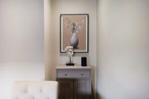 A framed artwork of a vase with flowers on a cabinet, a bust sculpture, and a black cylindrical object on the cabinet. - Cosy Keswick 1BR Sleeps 2 by Stay With Us (Keswick)