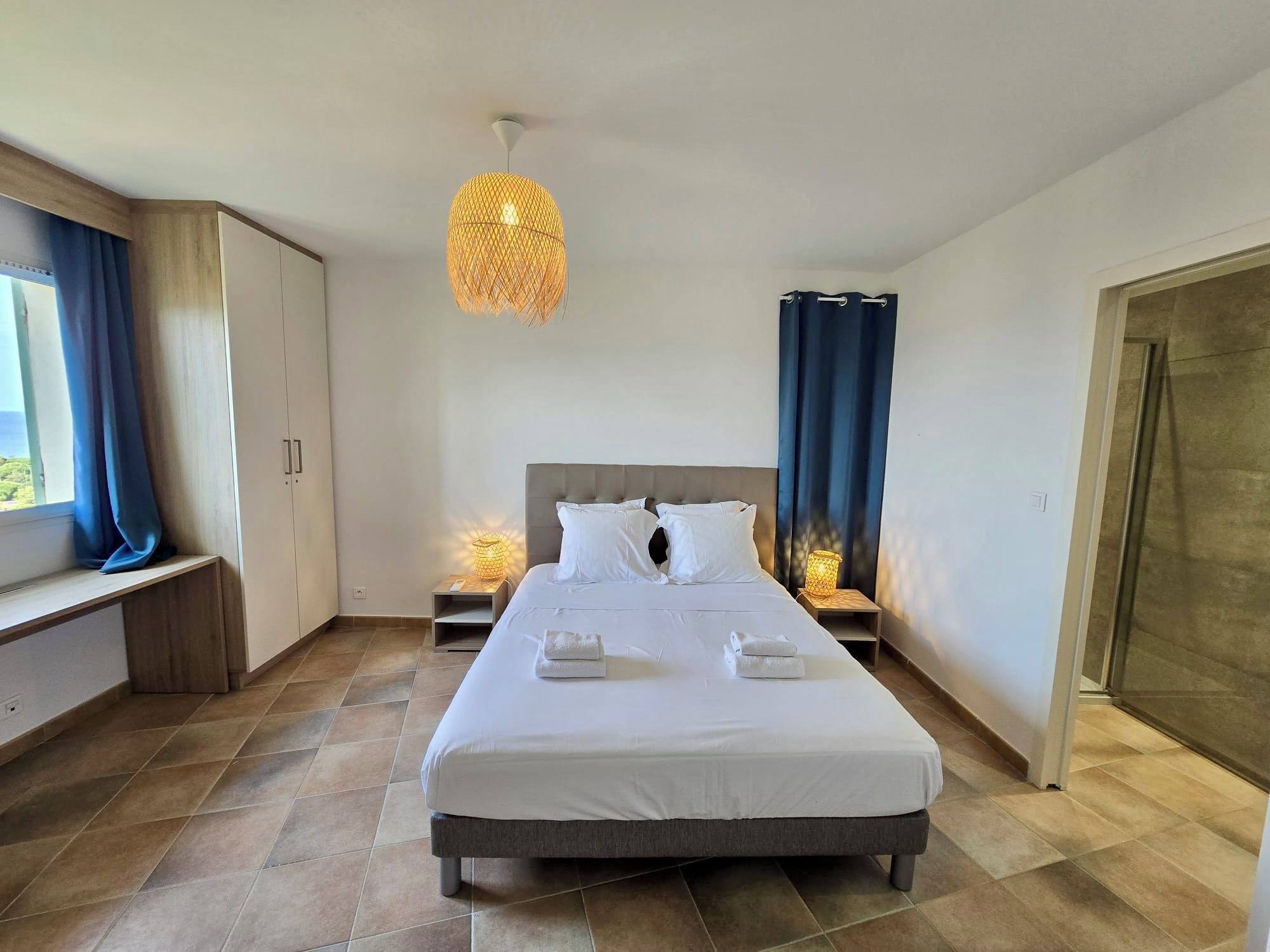 A hotel room with a bed, bedside lamps, a window with curtains, and a wardrobe.