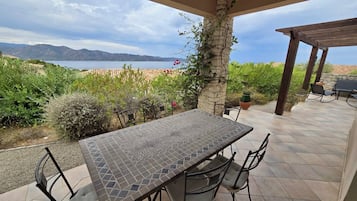 Eine Terrasse im Freien mit Tisch und Stühlen, mit Blick auf ein Gewässer und Berge.